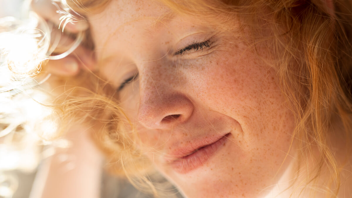 Redhead woman with closed eyes and sunspots on her face