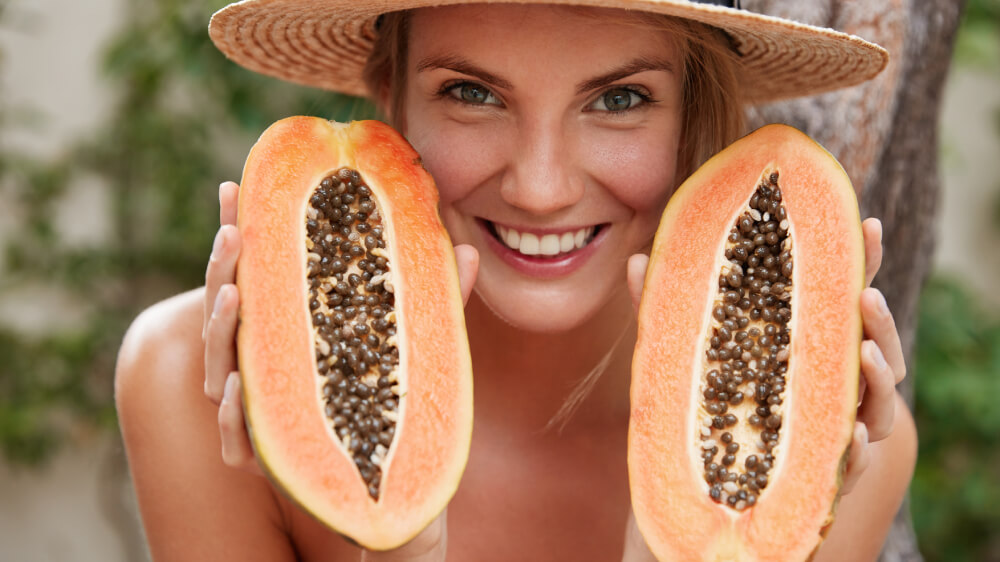 Portrait of glad woman wearing summer hat holding organic papaya